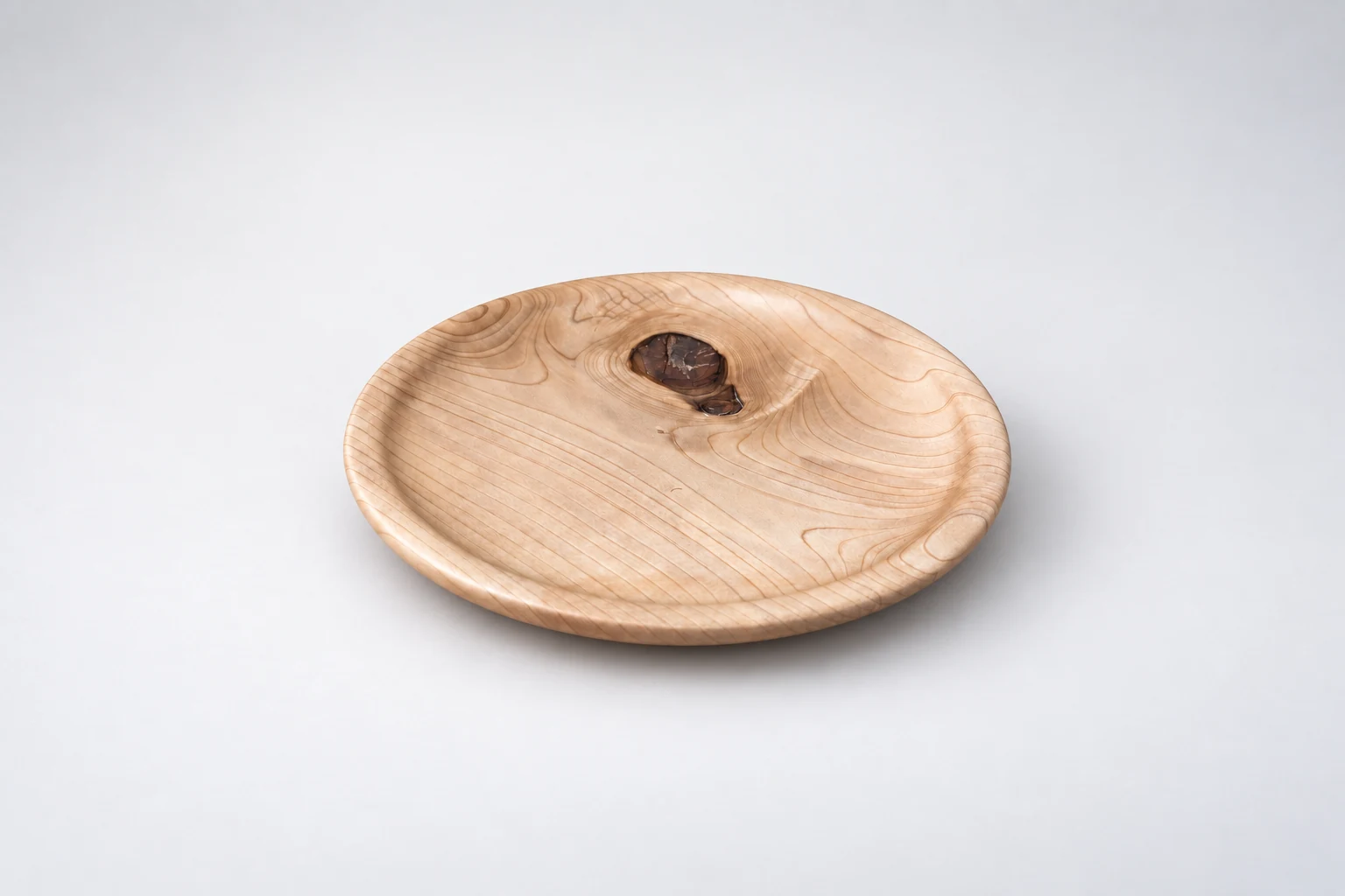 Shallow turned wooden plate with a dark knot near the rim